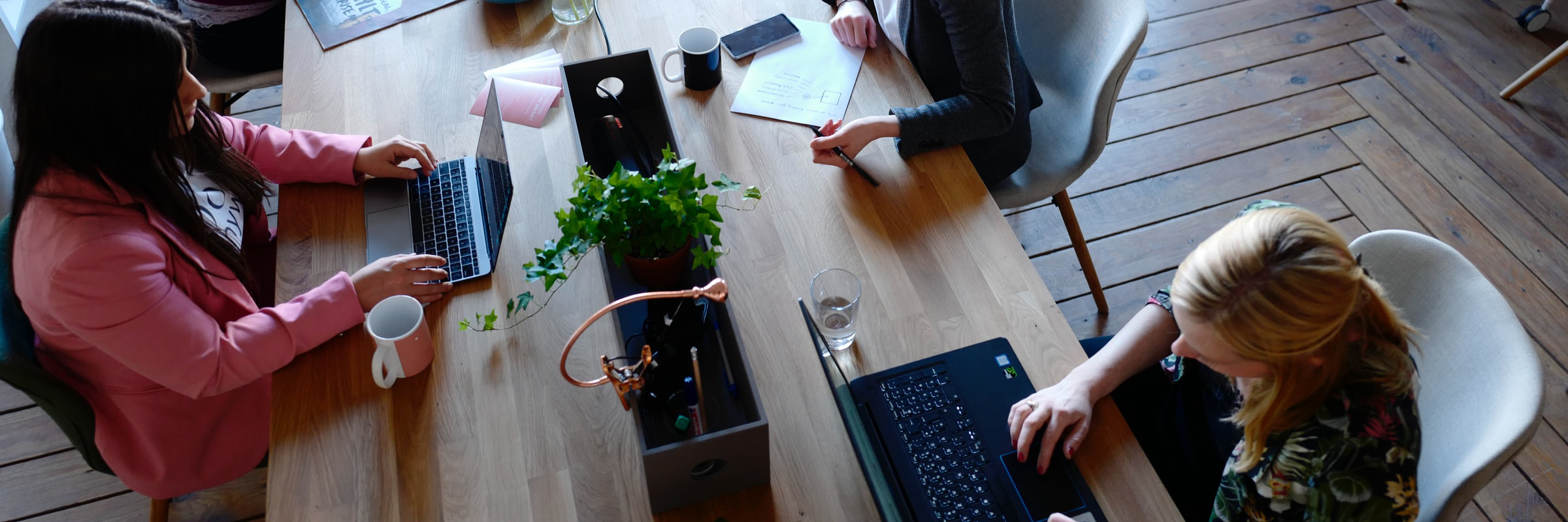 The picture shows a long table at which two women sit opposite each other and work on their laptops.